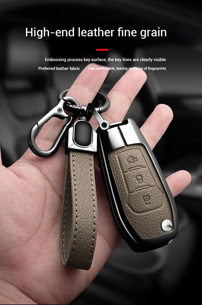 A hand holds a dark olive leather key fob cover with an aluminum alloy key, showing fine grain texture.