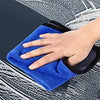 A hand is using a blue clay bar on a black foam applicator for car detailing.