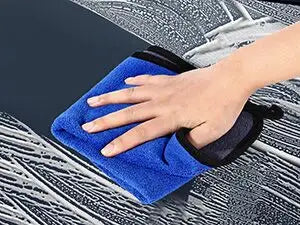 A hand is using a blue clay bar on a black foam applicator for car detailing.