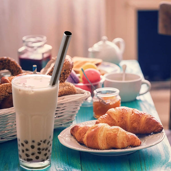 A glass of milk or smoothie is shown next to a basket of baked goods and a reusable stainless steel drinking straw set.