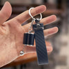 A hand holds a black textured keychain with silver hardware, designed for desk stress relief.