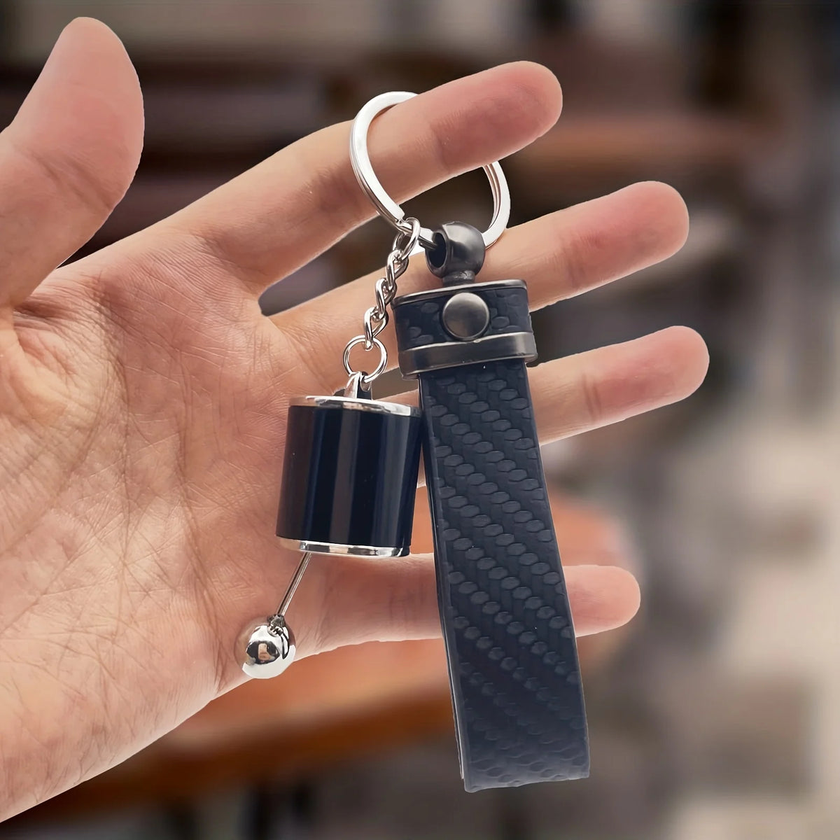 A hand holds a black textured keychain with silver hardware, designed for desk stress relief.
