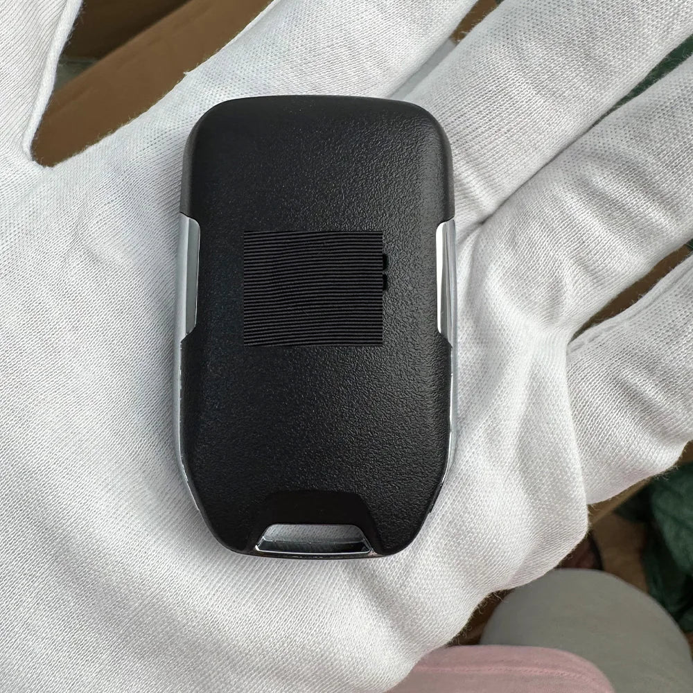 A black aftermarket remote key for a Chevrolet truck or SUV is held in a person's hand.