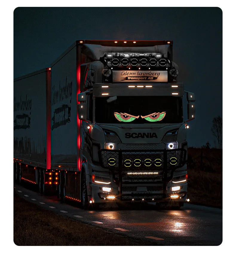 A Scania truck with an RGB dynamic demon eye light display shining brightly at night.