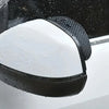 Black anti-fog textured covers placed over a vehicle's rearview mirror, with water droplets visible.