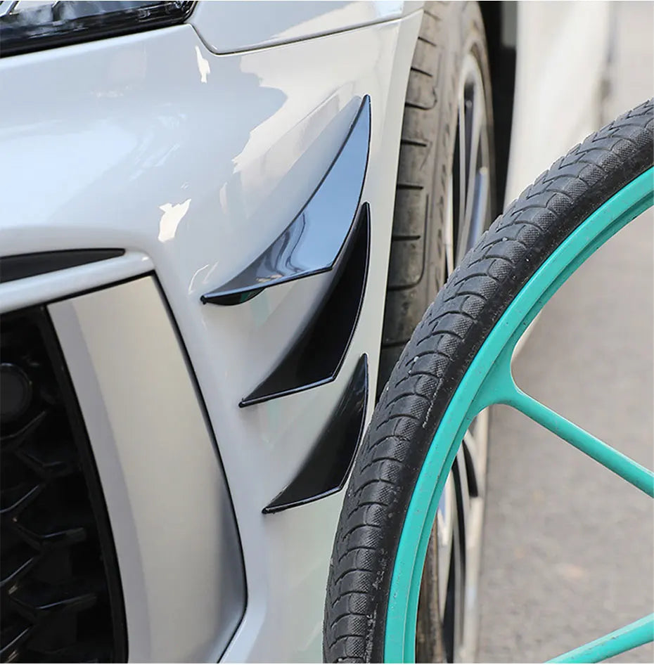 Close-up of black universal car spoiler fins installed on a white car bumper next to a tire.
