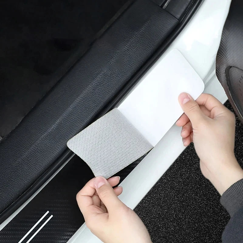 A hand is holding a white carbon fiber door sill protector against a black car door panel.