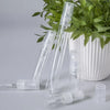 A set of clear glass perfume bottles with pump dispensers displayed in front of a potted green plant.