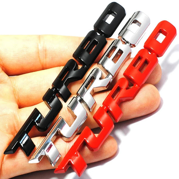 A hand holds several chrome and black metal alloy car modification badges.