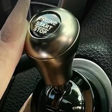 Close-up of an all-metal cylindrical car start stop button accessory on a vehicle interior.