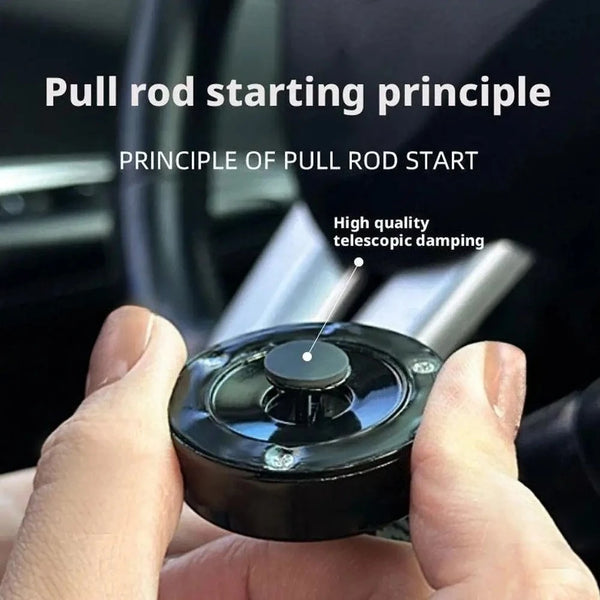 A hand holds an all-metal cylindrical car start button accessory demonstrating the pull rod starting principle.