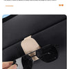 A hand holds a black magnetic leather sunglasses holder designed for car sun visors.