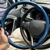 Eine Hand hält eine blau-schwarze Kohlefaser-Lenkradabdeckung im Innenraum eines Autos.