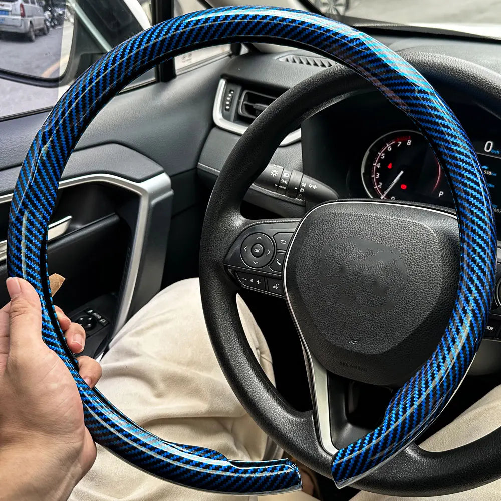 Eine Hand hält eine blau-schwarze Kohlefaser-Lenkradabdeckung im Innenraum eines Autos.