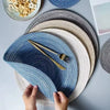 A hand is placing a blue and white striped cotton yarn placemat onto a gray table.