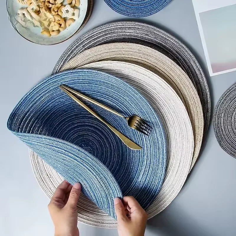 A hand is placing a blue and white striped cotton yarn placemat onto a gray table.