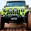 Three off-road vehicles, including a lime green Jeep, are parked on dirt terrain.