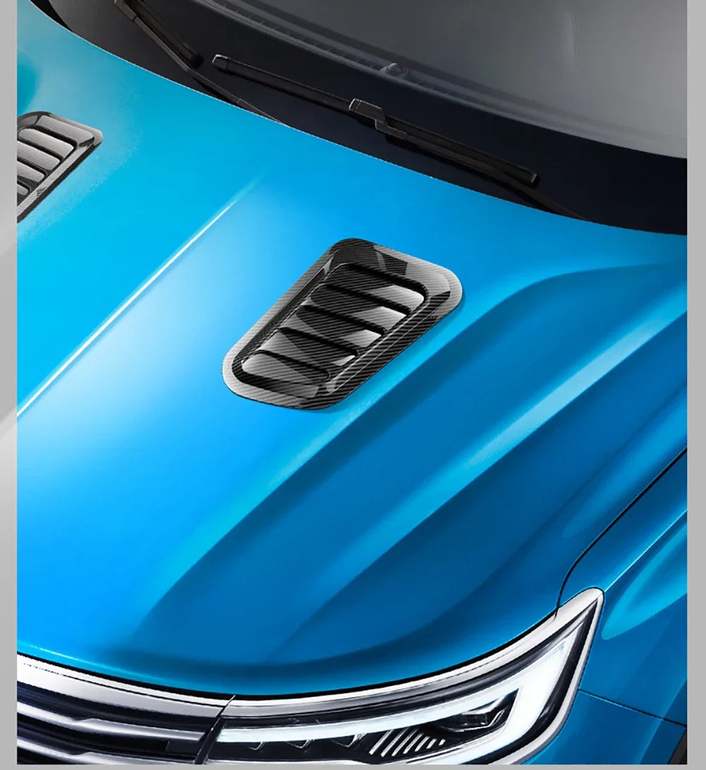 Close-up of a blue car hood featuring a black carbon fiber vent trim and chrome grille.