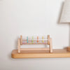 A wooden rainmaker musical toy with colorful plastic tubes mounted on a wooden frame.