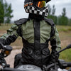 A person wearing a black and white checkered helmet and a green waterproof motorcycle raincoat sits on a motorcycle.