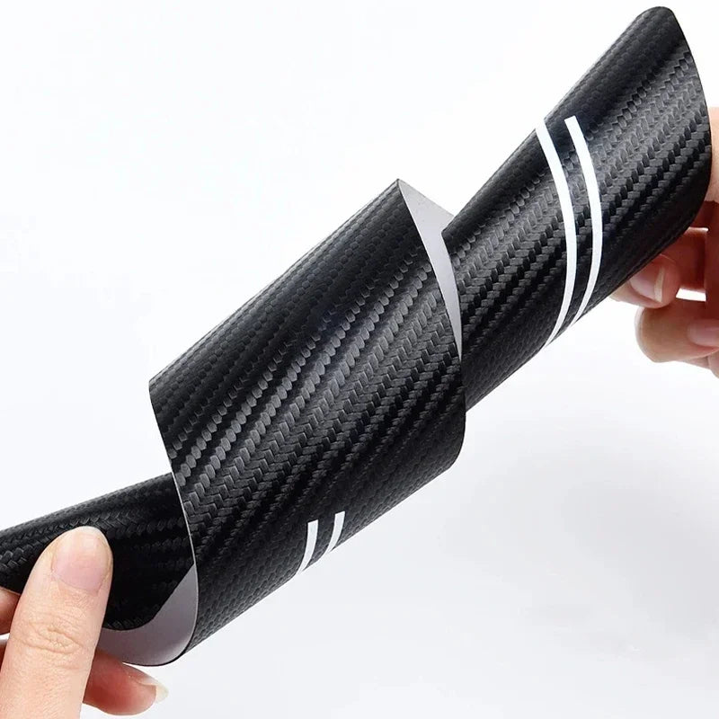 A close-up of a black carbon fiber door sill protection strip being held by a hand.