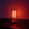 A glass cylindrical LED night light with glowing filaments rests on a metallic tray.
