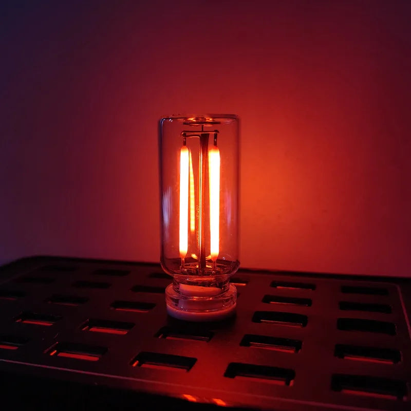 A glass cylindrical LED night light with glowing filaments rests on a metallic tray.