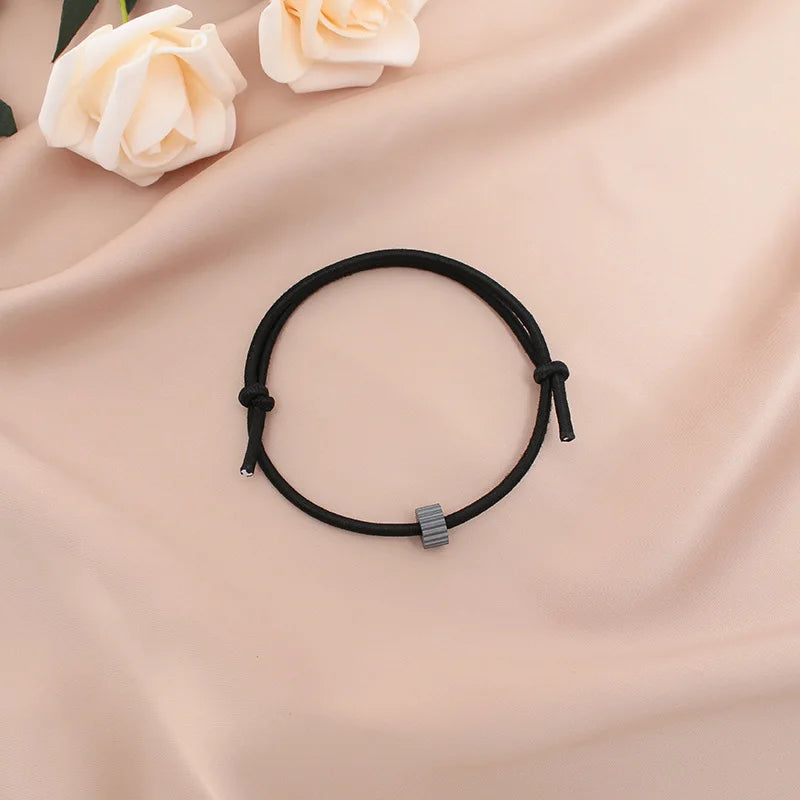 A black heart-shaped fitness tracker bracelet is displayed on a soft pink fabric next to white roses.