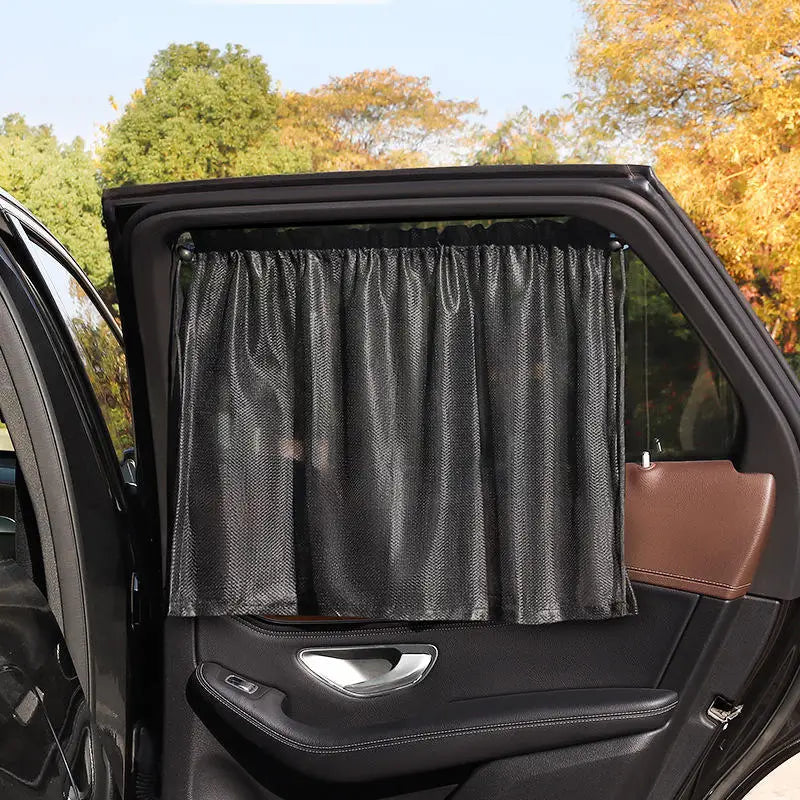 A black suction cup window sunshade is shown inside a car window, with green foliage visible outside.