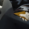 A hand wearing a light glove holds a yellow triangle squeegee tool against a dark car window.