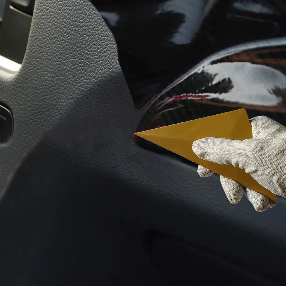 A hand wearing a light glove holds a yellow triangle squeegee tool against a dark car window.