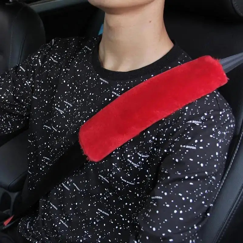 A person wearing a black patterned shirt with a red shoulder pad on a car seatbelt.
