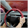 A hand grips a red perforated leather steering wheel grip on a car steering wheel.