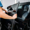 A person is applying or inspecting a premium car window tint film on a black vehicle.