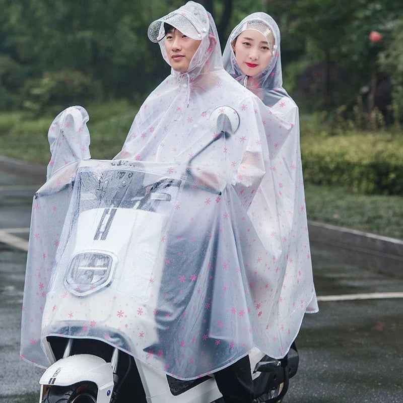 Two people wearing transparent windproof motorcycle rain ponchos riding a white motorcycle on a wet road.