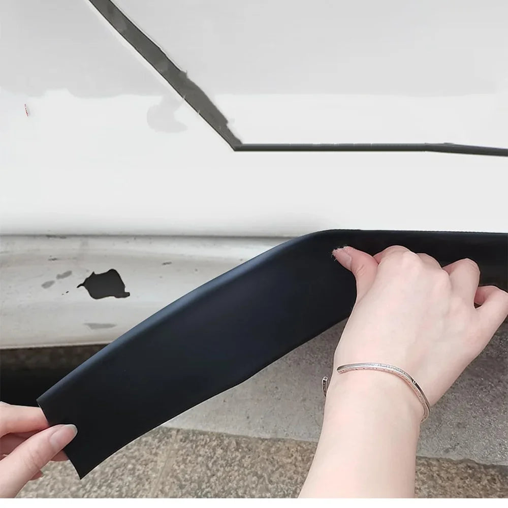 Eine Hand hält einen schwarzen, selbstklebenden Schutzstreifen für Autotüren gegen eine weiße Oberfläche.