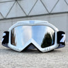 A pair of white windproof sports goggles with black accents resting on a gray concrete surface.