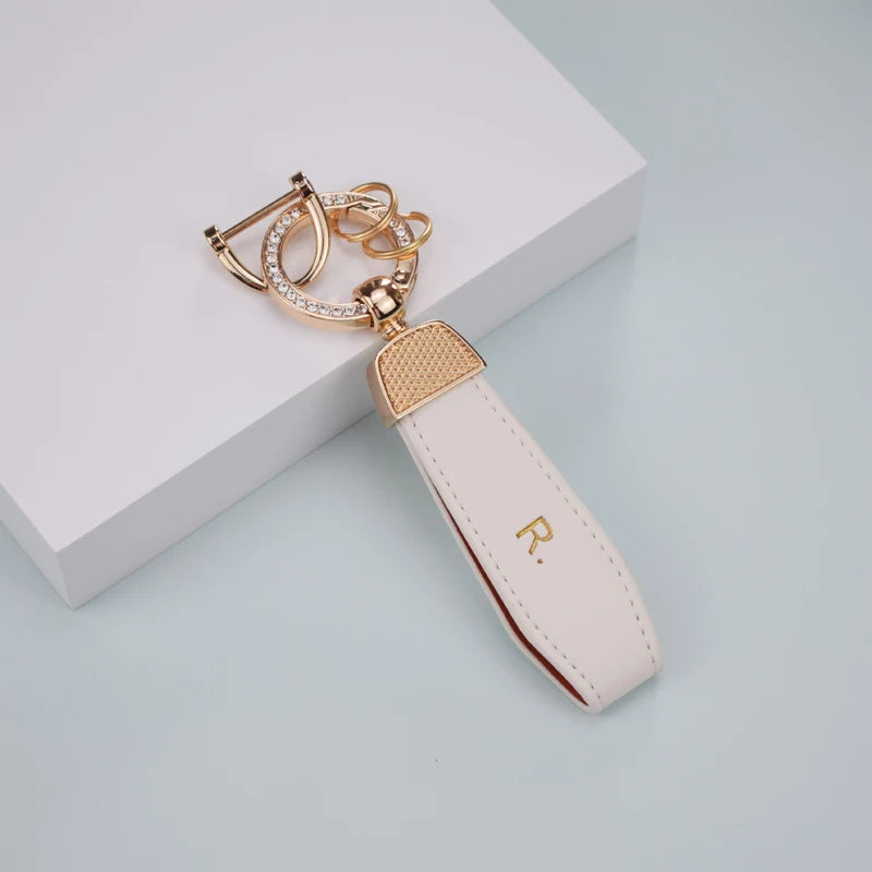 A light pink TPU car key fob cover with a gold-tone chain and sparkling accents, resting on a white surface.