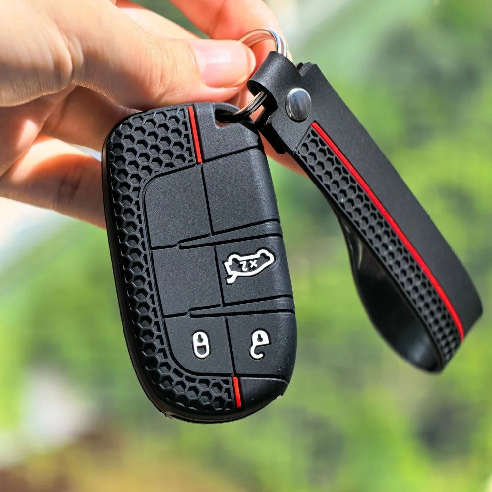 A black silicone car key cover with two keys attached to a keyring is being held by a hand against a blurred green background