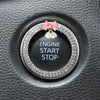 Close-up of a round black switch button trimmed with clear rhinestones and topped with a pink fabric bow and bell.