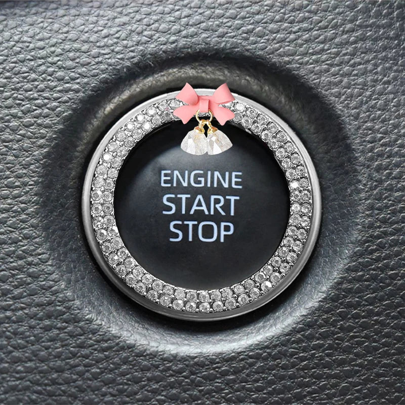 Close-up of a round black switch button trimmed with clear rhinestones and topped with a pink fabric bow and bell.