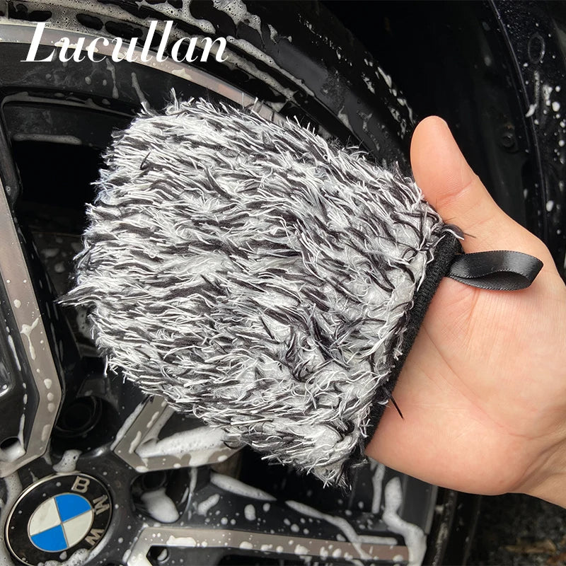 A hand holds a white microfiber wash mitt for wheel detailing, positioned near a black car wheel.