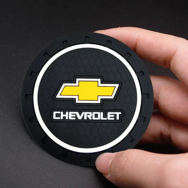 A hand holds a black car anti-slip coaster with a yellow Chevrolet emblem and white text.