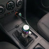 A close-up view of a universal aluminum gear shift knob installed in a vehicle's transmission tunnel.