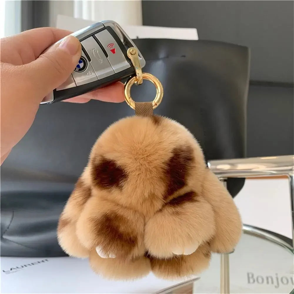 A fluffy brown bunny plush toy with a gold ring is being held by a hand against a dark background.