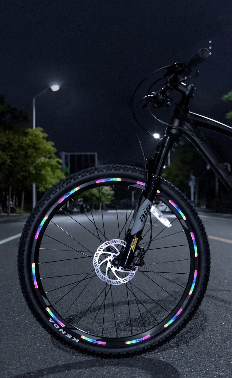 A black bicycle wheel with multi-color reflective safety stickers, photographed at night.