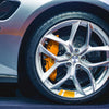 Close-up of a silver car wheel with an orange brake caliper and reflective safety stickers on the tire.