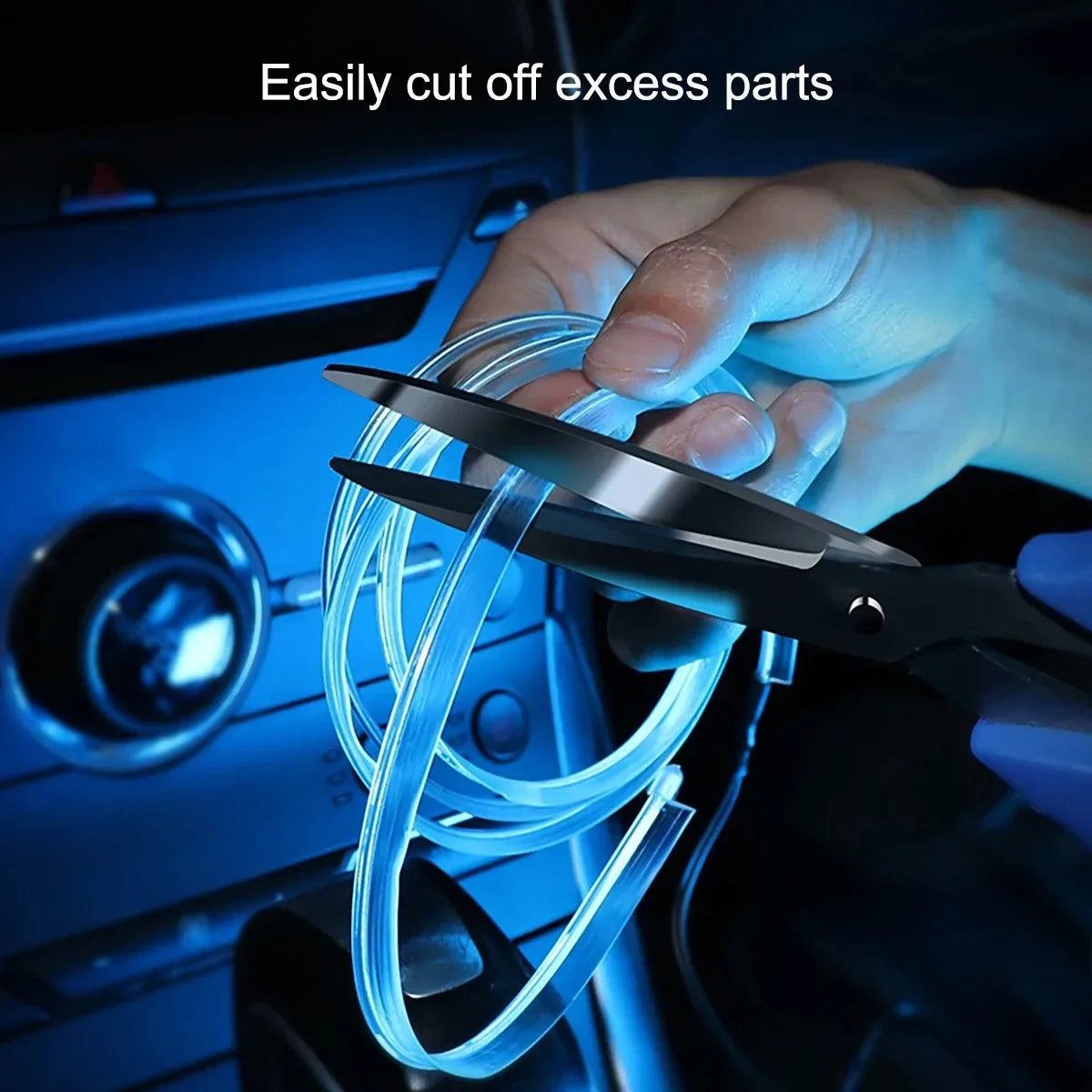 A hand uses a pair of scissors to cut excess parts of a flexible blue LED light strip for car interior decoration.