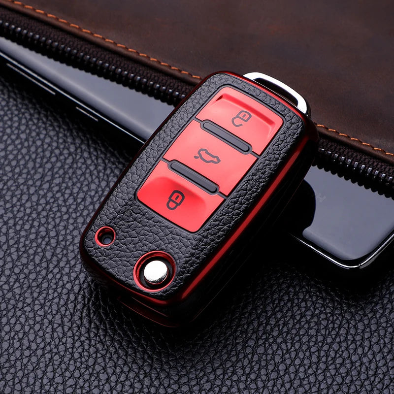 A black TPU leather car key case with red buttons is shown resting on a dark leather surface.