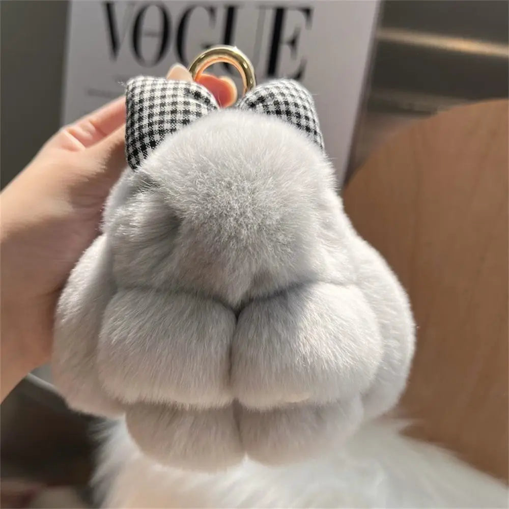 A close-up of a plush bunny keychain with soft gray fur and black checkered ears, held by a hand.